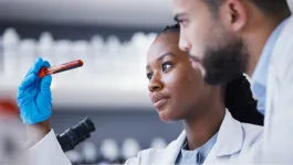 Pair of male and female workers in white coats in a laboratory intently study a test tube sample held by female