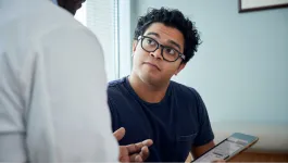 A woman in glasses listens intently during a sitting consultation with a doctor who is holding an iPad